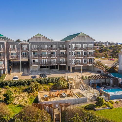 Cozy seaside condo complex with three stucco buildings, a central courtyard, pool, hot tub, and a fenced-in backyard area in sunny coastal terrain.
