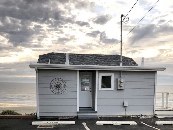 A small seaside building with a compass wall decoration, antennas and utility meters, under a cloudy sky.