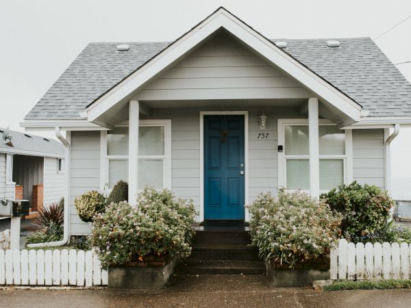 A front porch with white siding and pillars, a blue door numbered 757, and blooming shrubs in front.