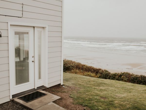 A foggy seaside view from a home porch, with a white door marked &ldquo;6,&rdquo; grass, and waves crashing offshore.