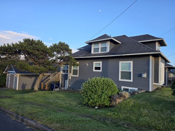 A sunny suburban house with blue siding, gabled roof, windows, and a green yard under a clear blue sky.