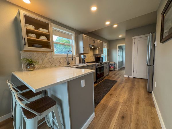 Bright modern kitchen with white cabinets, tiled backsplash, island with stools, stainless fridge, stove, and coffee maker.